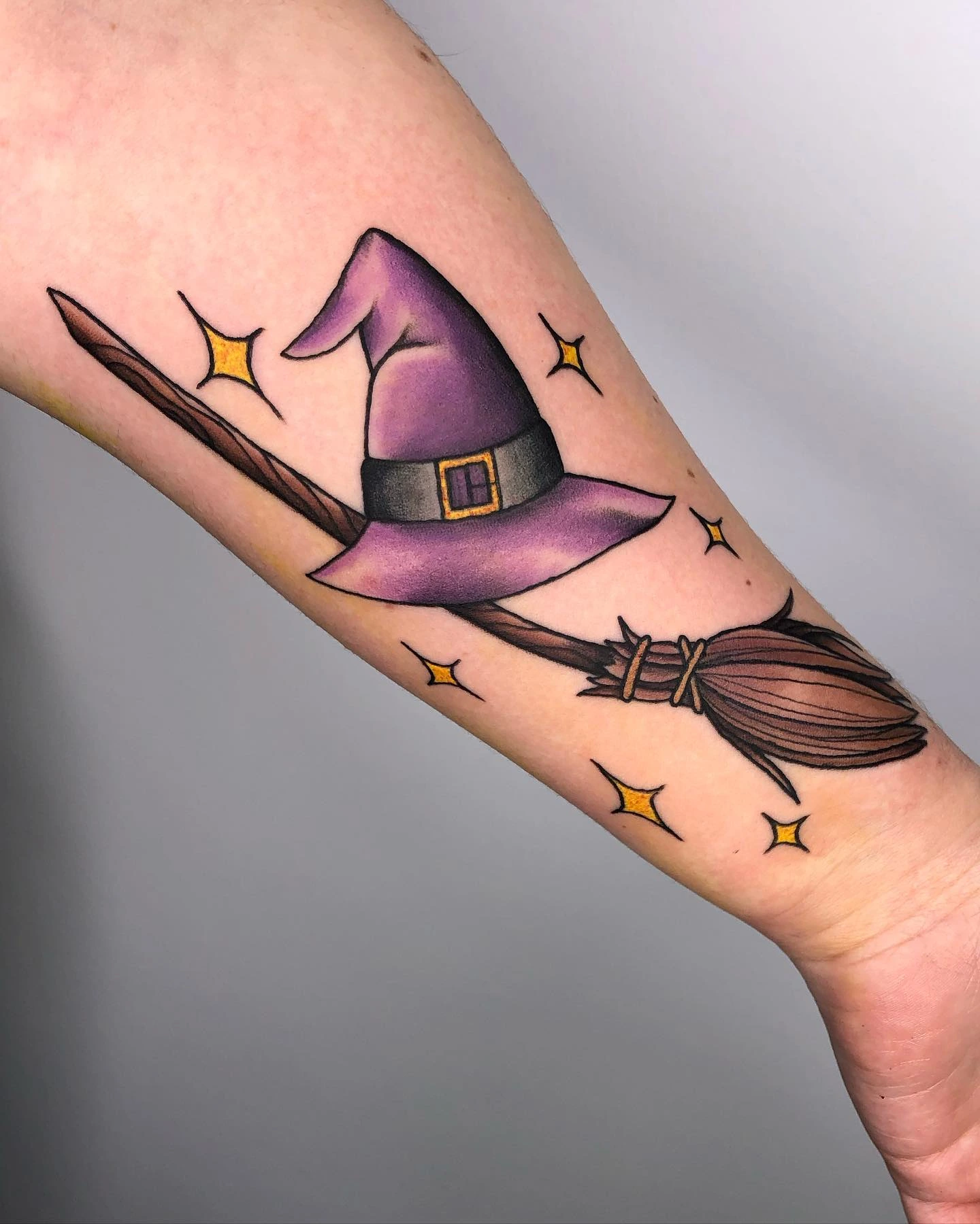 Purple witch hat resting on broomstick with gold sparkles