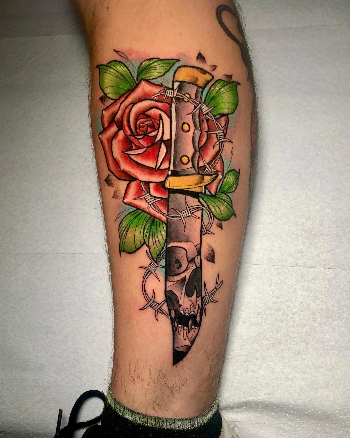 Dagger through a red rose with skull at the tip and barbed wire